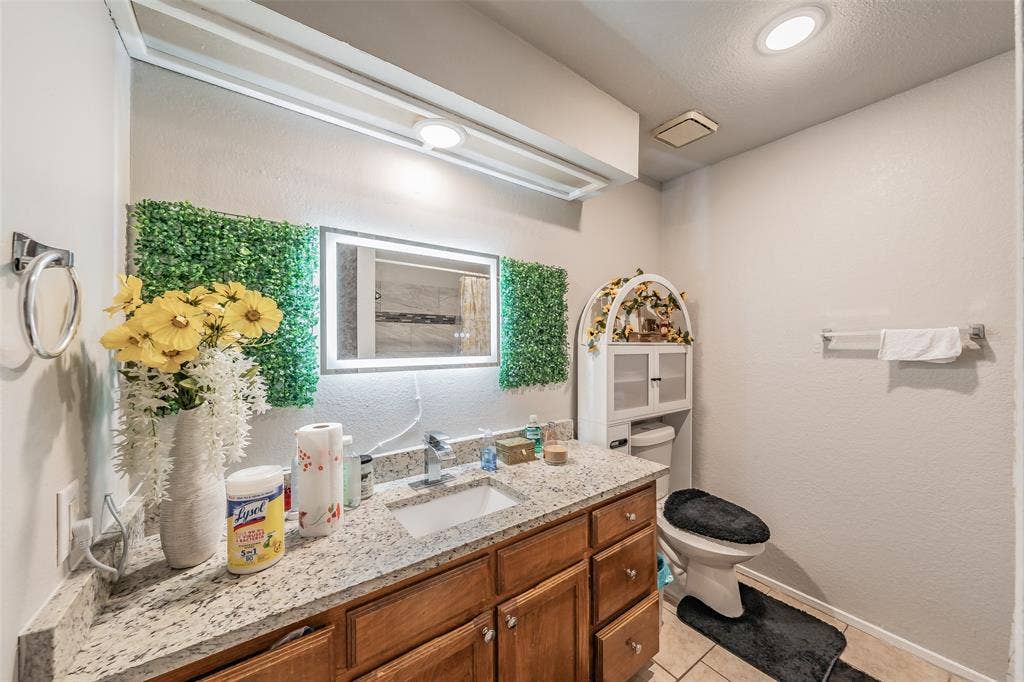 1126 Bathroom featuring a wood-finish vanity with a stone-composite countertop, integrated rectangular basin, chrome faucet, and a wall-mounted LED-backlit mirror