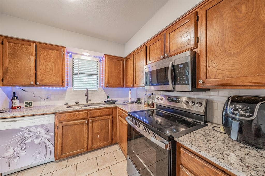1126 Kitchen featuring wood cabinetry, stone-finish countertops, subway tile backsplash, stainless steel microwave, and tile flooring