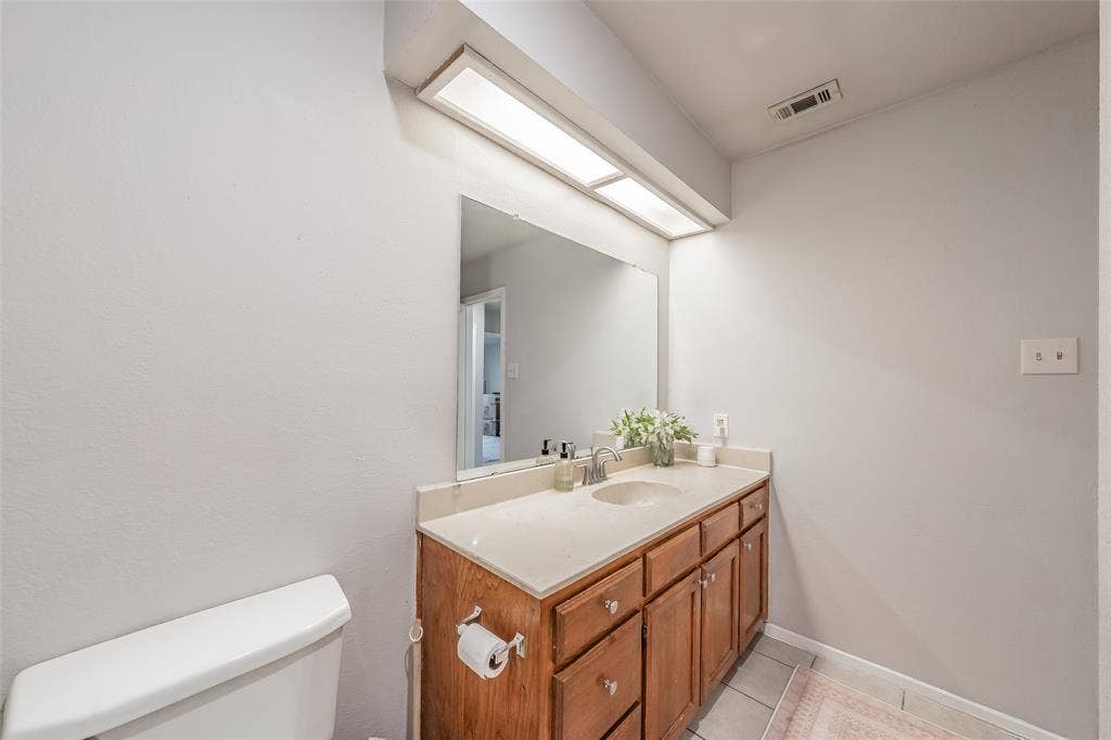 1128 Vanity featuring a light-toned countertop, an integrated sink basin, and wood-finish cabinetry with drawer and cabinet storage, paired with a large wall-mounted mirror and a linear overhead light fixture
