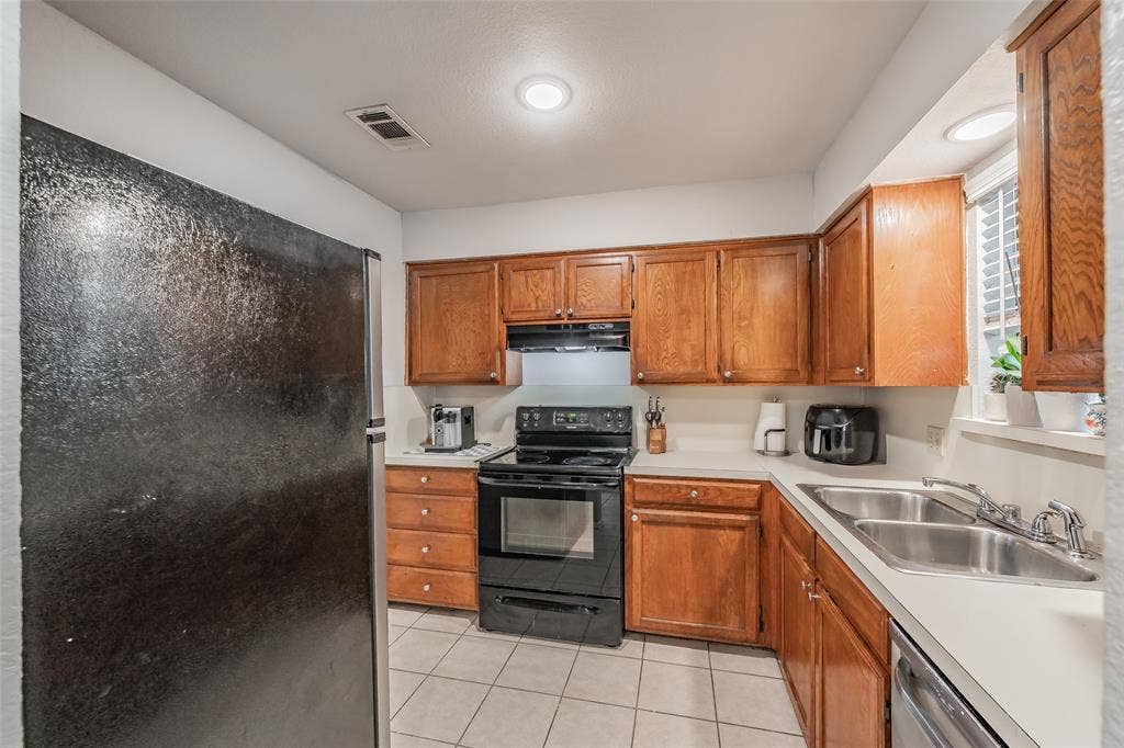 1128 Kitchen featuring stained wood cabinetry, solid-surface countertops, dual-basin stainless steel sink, black built-in oven range, and tile flooring