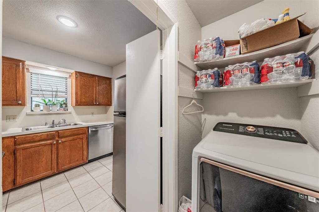 1128 Kitchen featuring wood cabinetry, stainless steel appliances, tile flooring, and a dedicated laundry area with built-in shelving