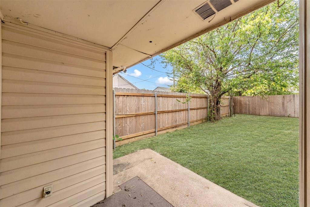 1126 Covered concrete patio with horizontal siding exterior, expansive lawn, and perimeter wood privacy fencing