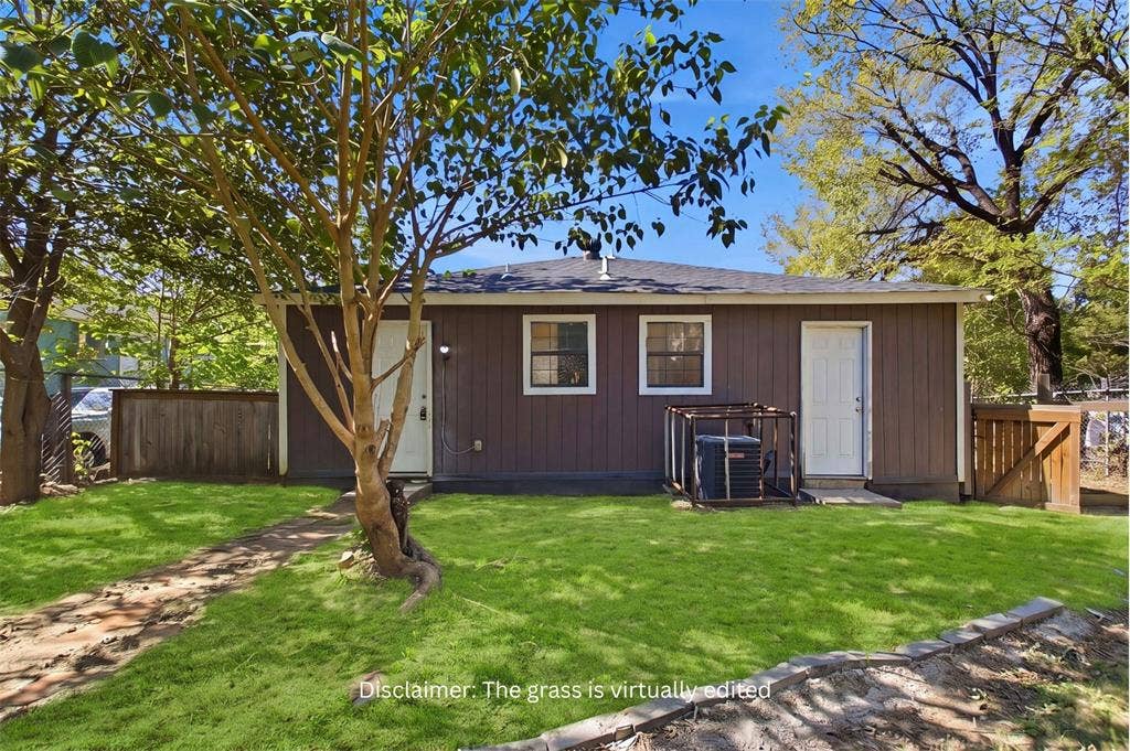 Exterior view featuring vertical wood-finish siding, a composition shingle roof, two white-frame entry doors, and a fenced backyard