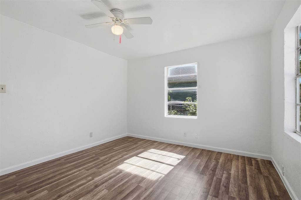 Room featuring wood-finish flooring, white walls, two windows, and a ceiling-mounted fan with integrated light