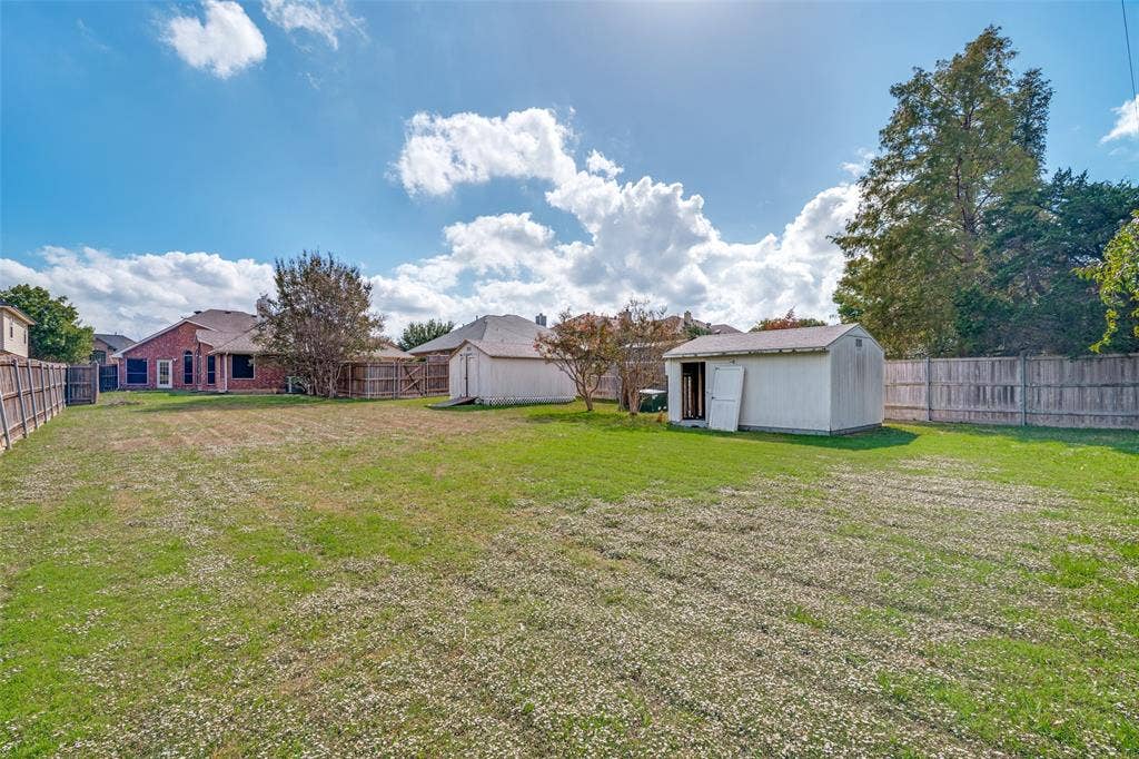 1909 Blackfoot Trail, Mesquite, TX 75149 Expansive backyard featuring a large grass lawn, perimeter wood fencing, and two detached storage structures