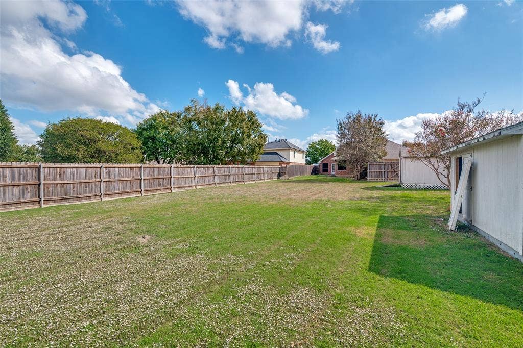 1909 Blackfoot Trail, Mesquite, TX 75149 Expansive backyard featuring a natural grass lawn, full-perimeter wood fencing, and a detached storage structure