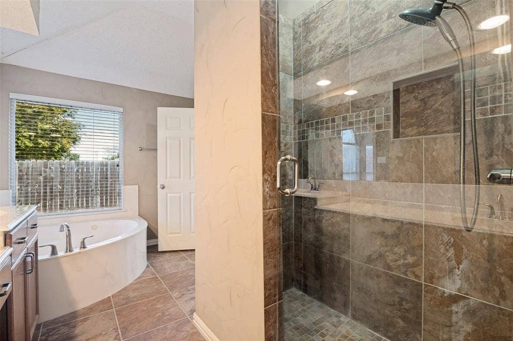 1909 Blackfoot Trail, Mesquite, TX 75149 Walk-in shower with stone-tile surround, glass enclosure, and built-in recessed niche; deep soaking jetted tub; tile flooring; and wood-finish cabinetry