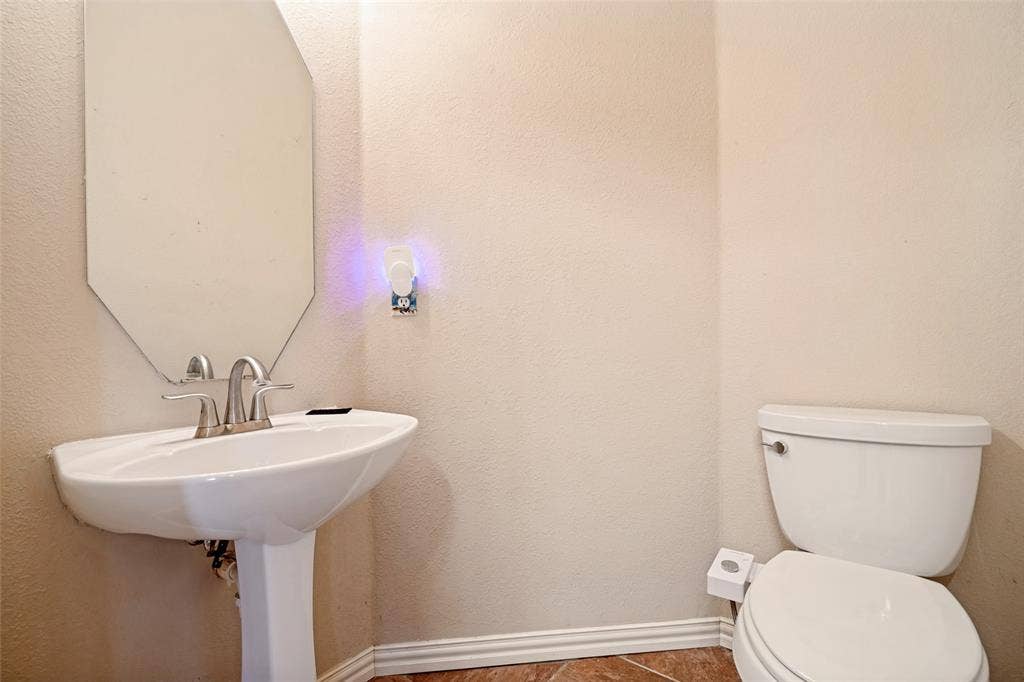 1909 Blackfoot Trail, Mesquite, TX 75149 Pedestal sink with a dual-handle faucet, wall-mounted octagonal mirror, and ceramic toilet