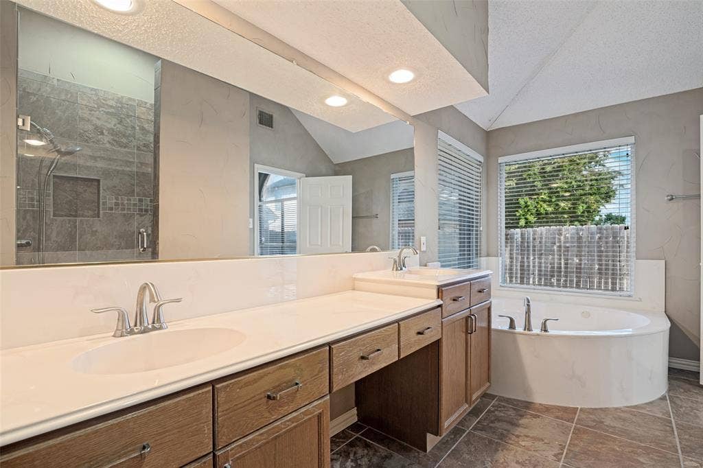 1909 Blackfoot Trail, Mesquite, TX 75149 Dual-sink vanity with wood cabinetry and light-toned solid surface countertops, glass-enclosed walk-in shower with tiled surround, and jetted soaking tub