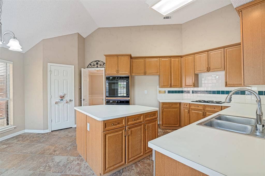 1909 Blackfoot Trail, Mesquite, TX 75149 Kitchen featuring wood cabinetry, central island with surface workspace, built-in double oven, gas cooktop, and tile flooring with vaulted ceiling