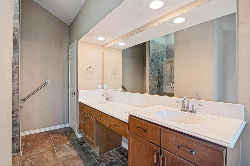 1909 Blackfoot Trail, Mesquite, TX 75149 Dual-vanity cabinet with white solid-surface countertop and integrated sinks, full-width wall mirror, recessed lighting, and tile flooring