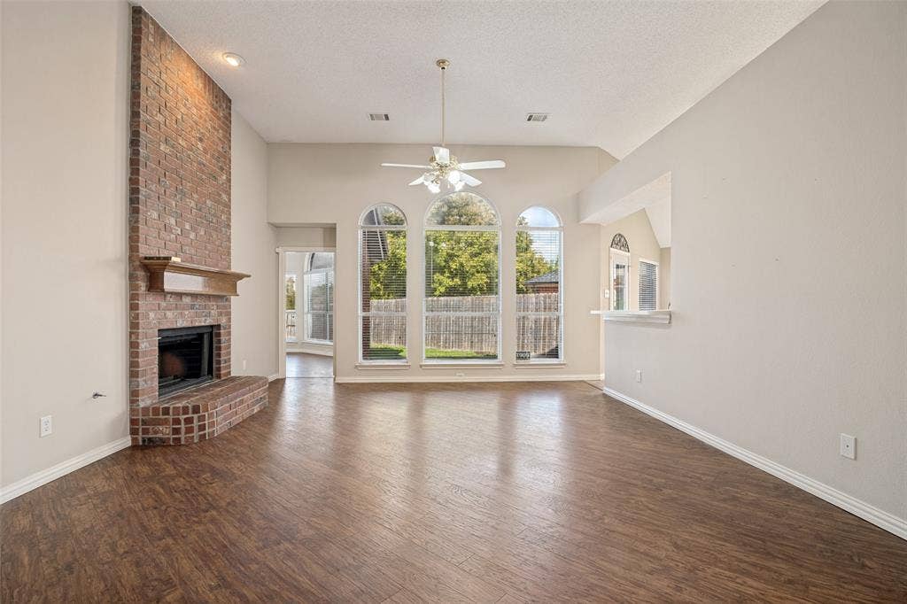 1909 Blackfoot Trail, Mesquite, TX 75149 High-ceilinged living area featuring wood-finish flooring, a floor-to-ceiling brick fireplace with a wood mantel, and arched windows