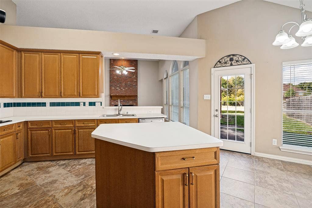 1909 Blackfoot Trail, Mesquite, TX 75149 Kitchen featuring wood cabinetry, a central island with a solid surface countertop, a red brick fireplace, tile flooring, and a glass-paneled exterior door with arched decorative ironwork