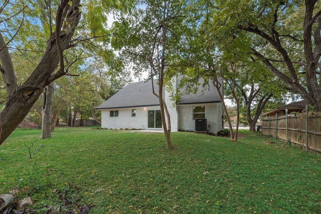 5614 University Hills Boulevard, Dallas, TX 75241 Backyard featuring a painted brick exterior, steep-pitched roofline, mature trees, and a wooden privacy fence