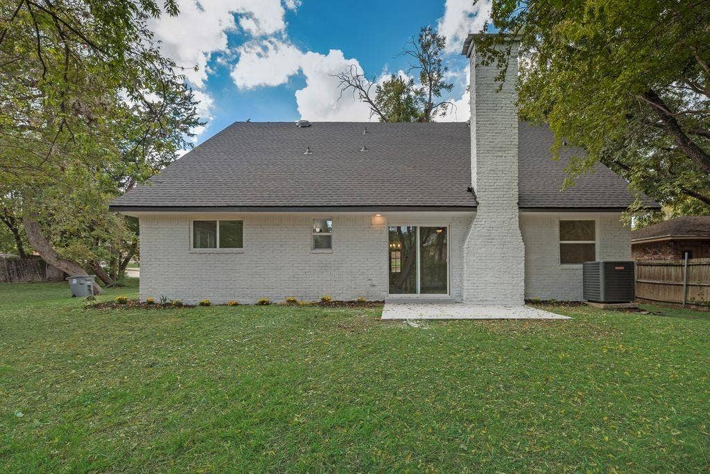 5614 University Hills Boulevard, Dallas, TX 75241 Painted brick exterior featuring a prominent masonry chimney, sliding glass doors, and a concrete patio