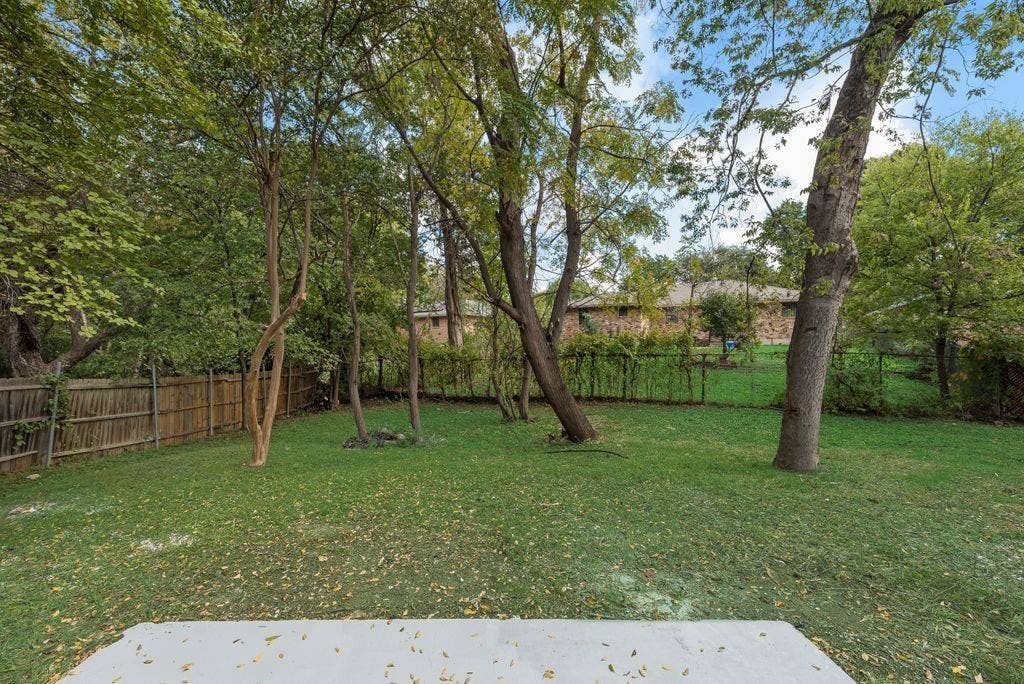 5614 University Hills Boulevard, Dallas, TX 75241 Spacious backyard featuring a concrete patio, mature trees, and perimeter wood fencing