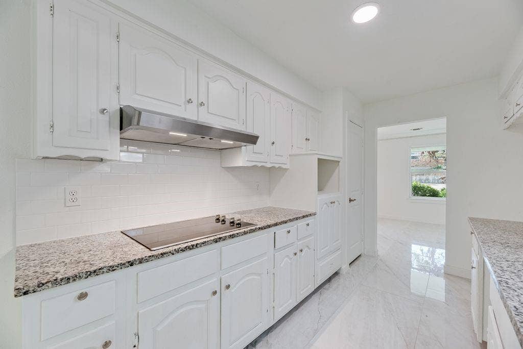 5614 University Hills Boulevard, Dallas, TX 75241 Kitchen featuring white cabinetry, stone-finish countertops, subway tile backsplash, stainless steel range hood, and large-format tile flooring
