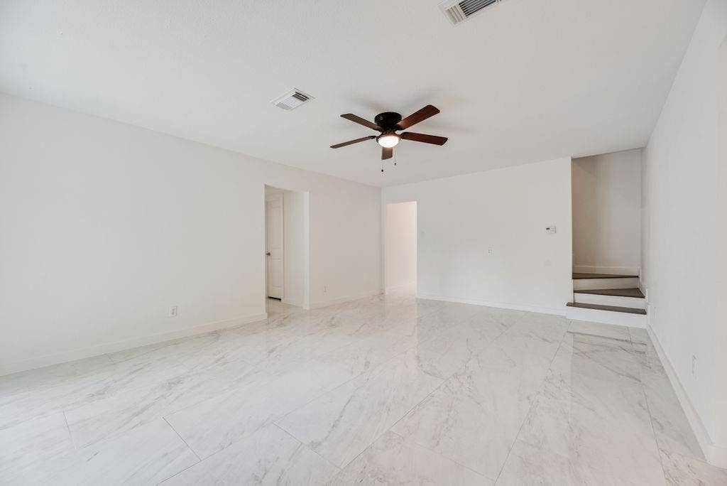 5614 University Hills Boulevard, Dallas, TX 75241 Open-concept interior featuring large-format tile flooring with a neutral veining pattern, a central multi-blade ceiling fan, and architectural staircase steps with dark-finish treads