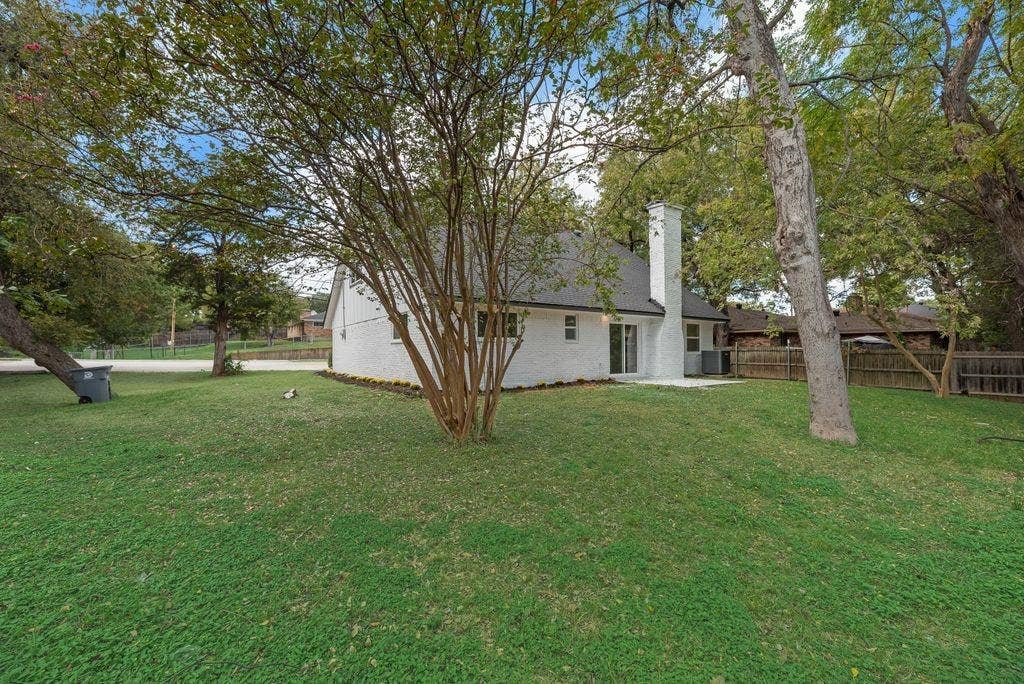 5614 University Hills Boulevard, Dallas, TX 75241 Exterior white-painted brick facade, gabled roofline, central chimney, sliding glass door, and expansive backyard with mature trees