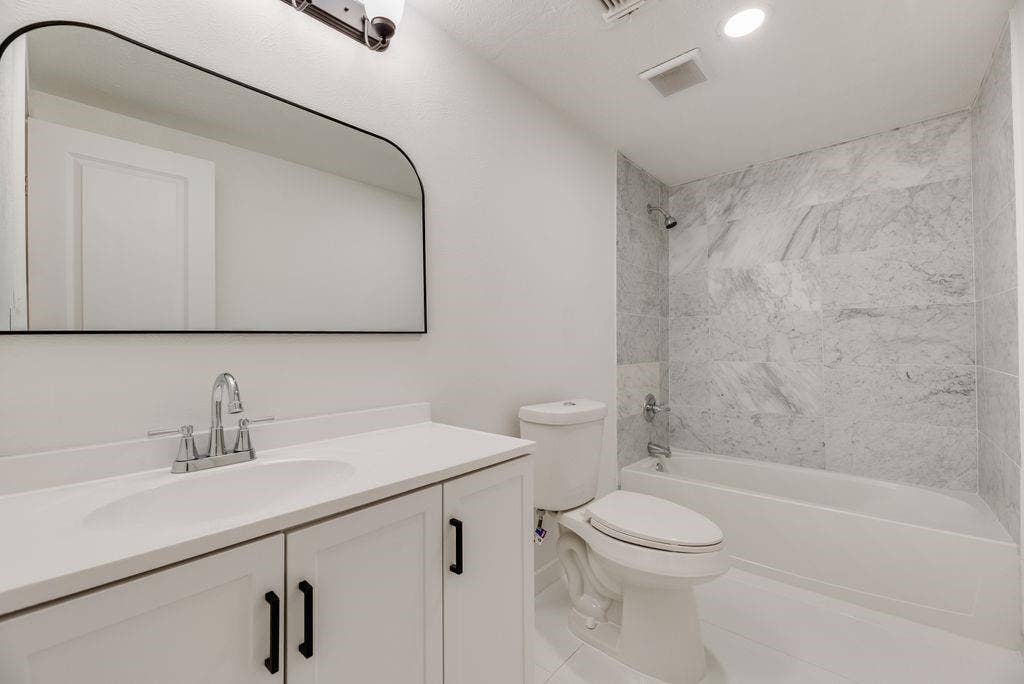 5614 University Hills Boulevard, Dallas, TX 75241 Bathroom featuring a vanity with a white countertop and integrated sink, arch-top wall mirror, matte black hardware, and a tub with surround tile