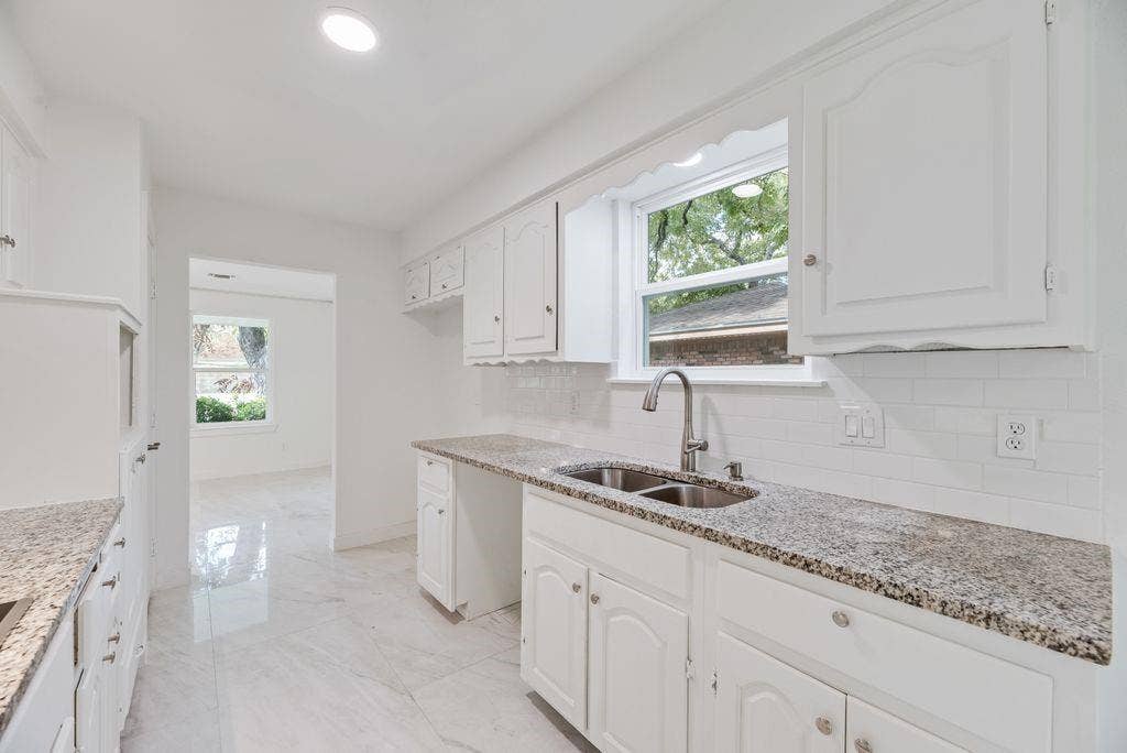5614 University Hills Boulevard, Dallas, TX 75241 Kitchen featuring white cabinetry, stone-finish countertops, subway tile backsplash, dual-basin stainless steel sink with gooseneck faucet, and light-tone tile flooring