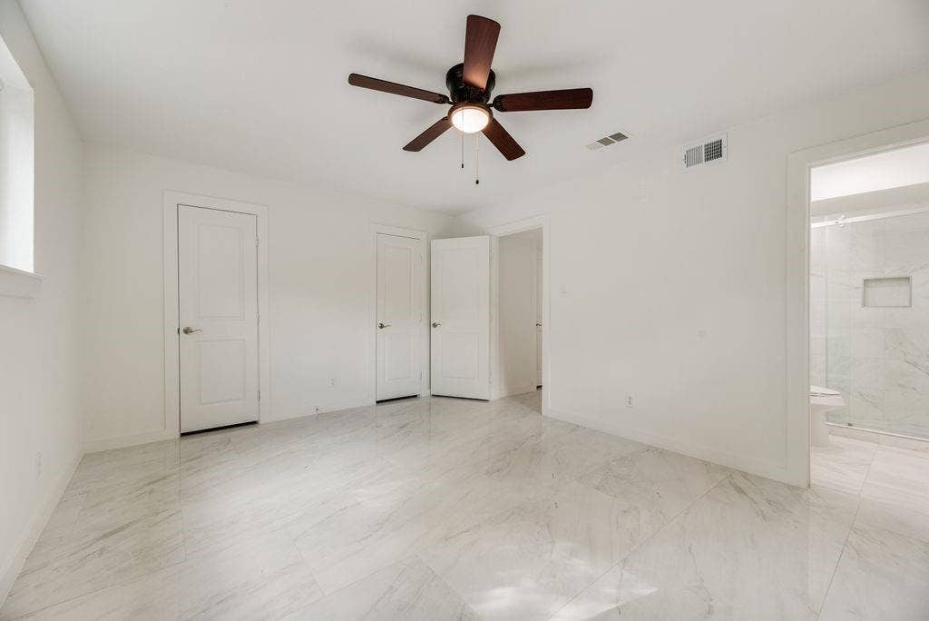 5614 University Hills Boulevard, Dallas, TX 75241 Primary Bedroom 2, Spacious room featuring large-format stone-style flooring, a central ceiling fan with integrated lighting, and three panel doors