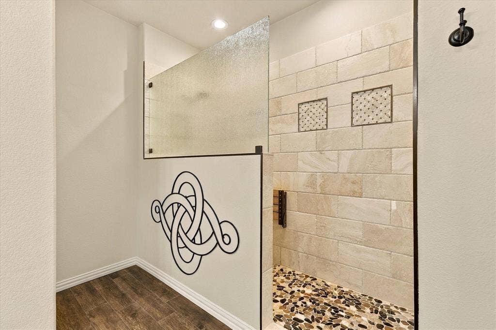 Indulge in a spa-like experience with this custom 8 foot walk-in shower, featuring beautiful tilework, a pebble stone floor, and sleek frameless glass.