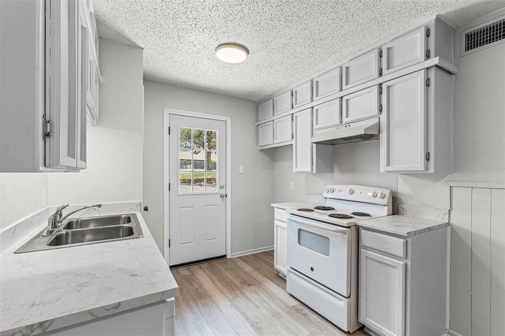 Kitchen featuring white electric range, a textured ceiling, light countertops, under cabinet range hood, and light wood-style flooring