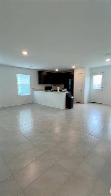 Open-concept interior featuring large-format tile flooring, recessed ceiling lighting, kitchen with dark cabinetry, stone-surface breakfast bar, and panel-style entry door