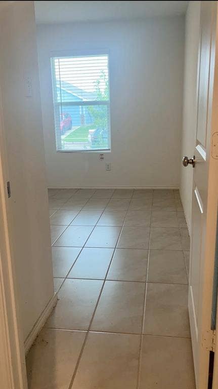 Interior space featuring large-format ceramic tile flooring, a single-pane window, and a standard swinging door with a metallic knob