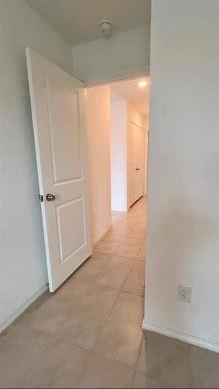 Interior corridor featuring light-toned tile flooring, white two-panel doors, and recessed lighting