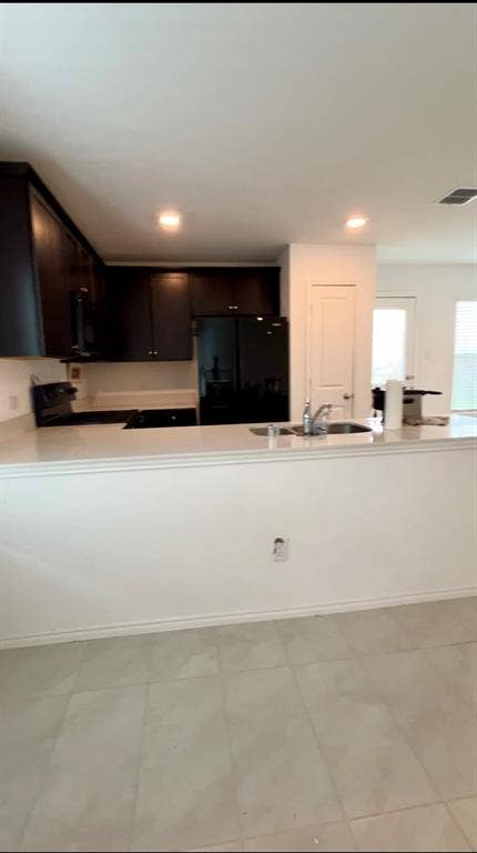 Kitchen featuring dark wood cabinetry, solid surface countertops, a stainless steel sink with a chrome faucet, and tiled flooring