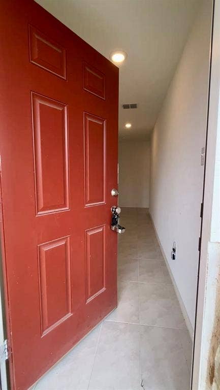 Red six-panel entry door with metallic hardware, large-format tile flooring, and recessed ceiling lighting