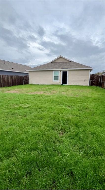 Backyard featuring a grass lawn, perimeter wood fencing, and a gable roof exterior