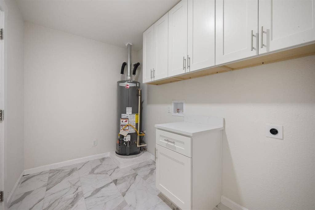Utility area featuring white shaker-style wall and base cabinetry, light-toned stone-finish countertop, and large-format tile flooring