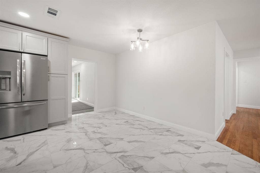 Large-format tile flooring, stainless steel French door refrigerator, white shaker-style cabinetry, and a multi-arm chandelier