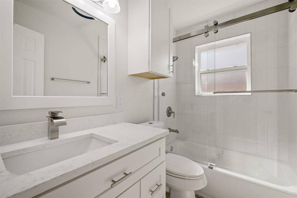 Bathroom featuring a white vanity with a composite countertop, undermount sink, sliding glass shower enclosure, and white wall-mounted cabinetry