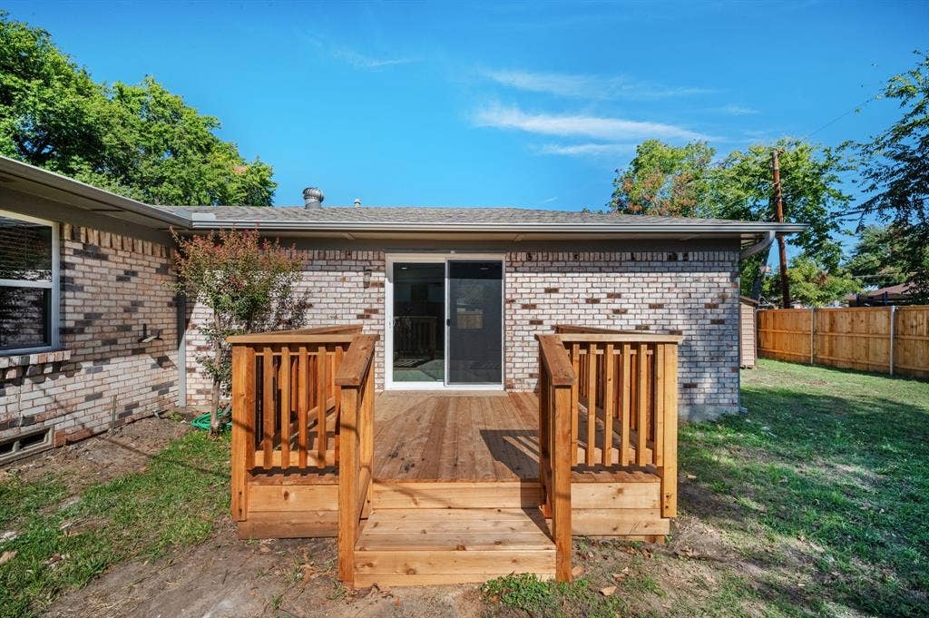 Exterior features include a brick façade, a wood-decked patio with stairs, sliding glass doors, and perimeter wood fencing