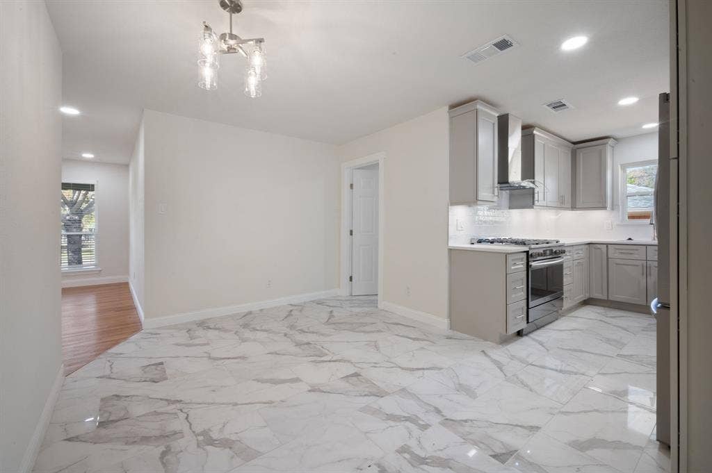 Kitchen featuring large-format tile flooring with marble-pattern veining, shaker-style cabinetry, stainless steel gas range, built-in range hood, and recessed lighting