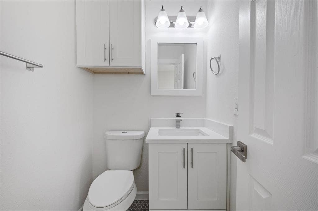 White cabinetry, vanity with integrated countertop, three-light fixture, wall-mounted mirror, and hexagonal floor tile