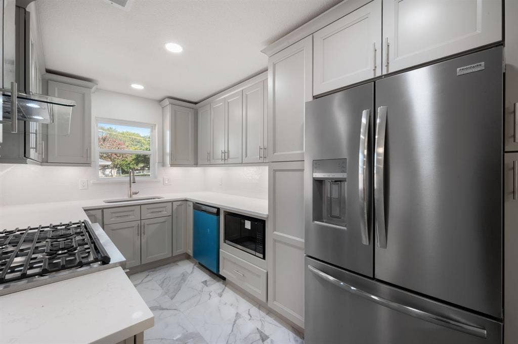 Kitchen featuring shaker-style cabinetry, solid-surface countertops, recessed lighting, stone-finish flooring, and stainless steel appliances