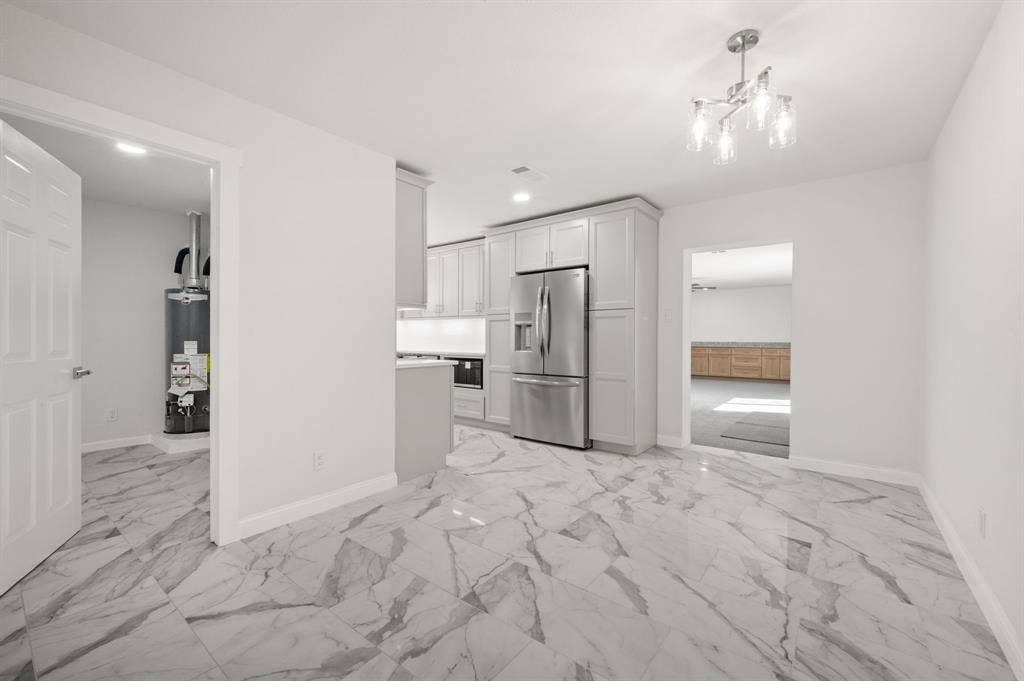 Kitchen featuring stone-pattern tile flooring, shaker-style cabinetry, stainless steel refrigerator, and polished multi-light chandelier