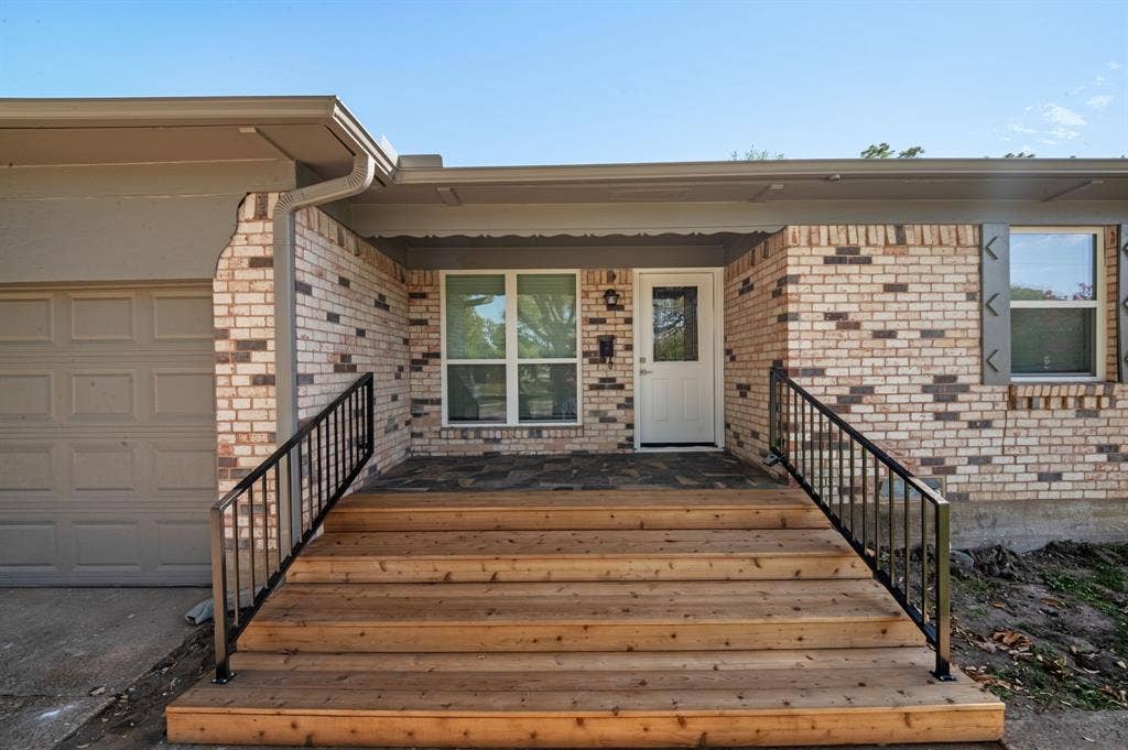 Brick exterior featuring natural wood-finish front steps, flagstone porch flooring, and black metal handrails