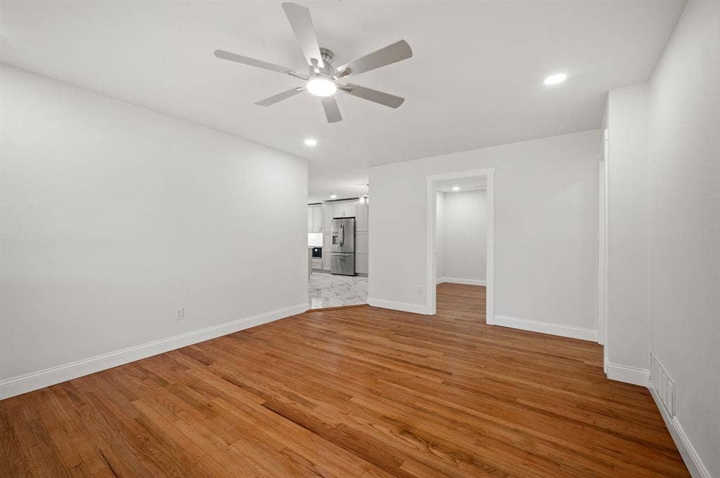 Neutral interior space featuring wood-finish flooring, a multi-blade ceiling fan with integrated lighting, and recessed overhead illumination