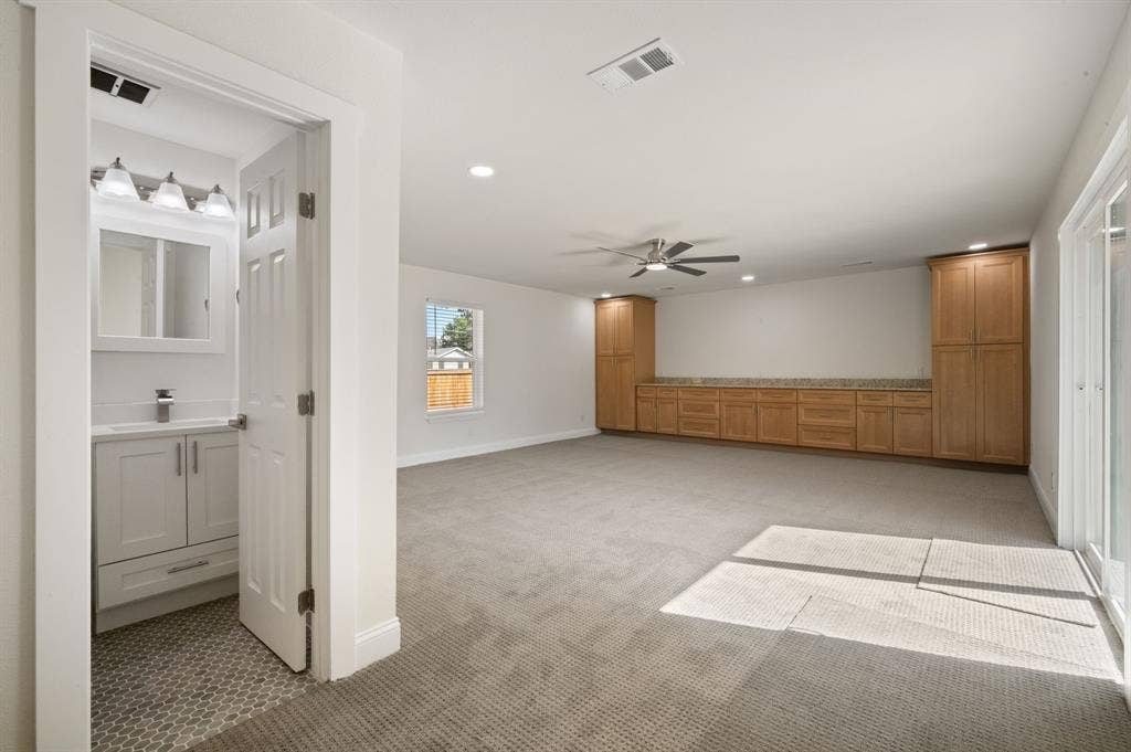 Room featuring wall-to-wall carpeting, extensive built-in cabinetry with stone-finish countertops, recessed lighting, and a bathroom containing a vanity with a sink and a decorative tile floor