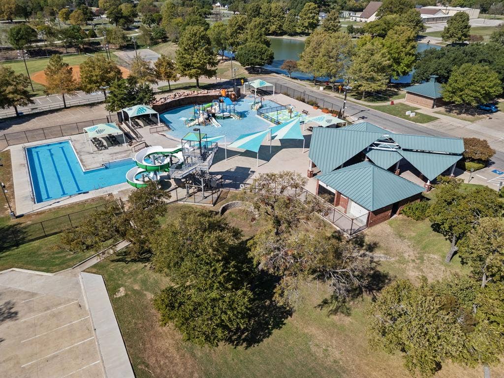 Community aquatic facility featuring a lap pool, water slide, splash pad, shaded structures, and metal roofing