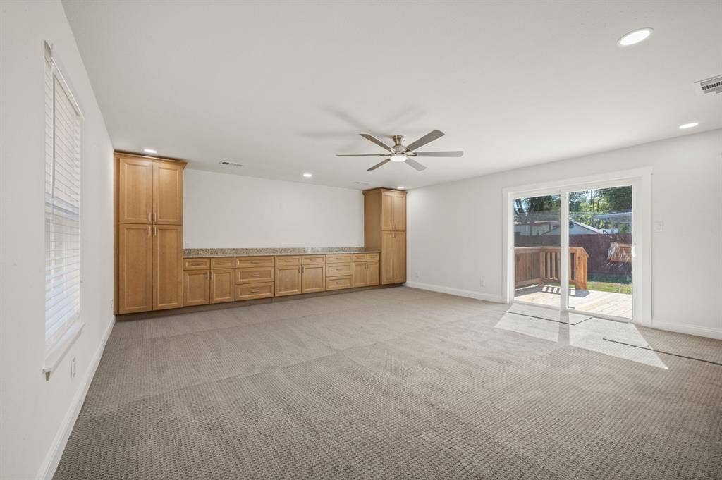 Built-in light wood cabinetry with stone countertop, ceiling fan with integrated lighting, recessed lighting, and glass sliding doors providing exterior access