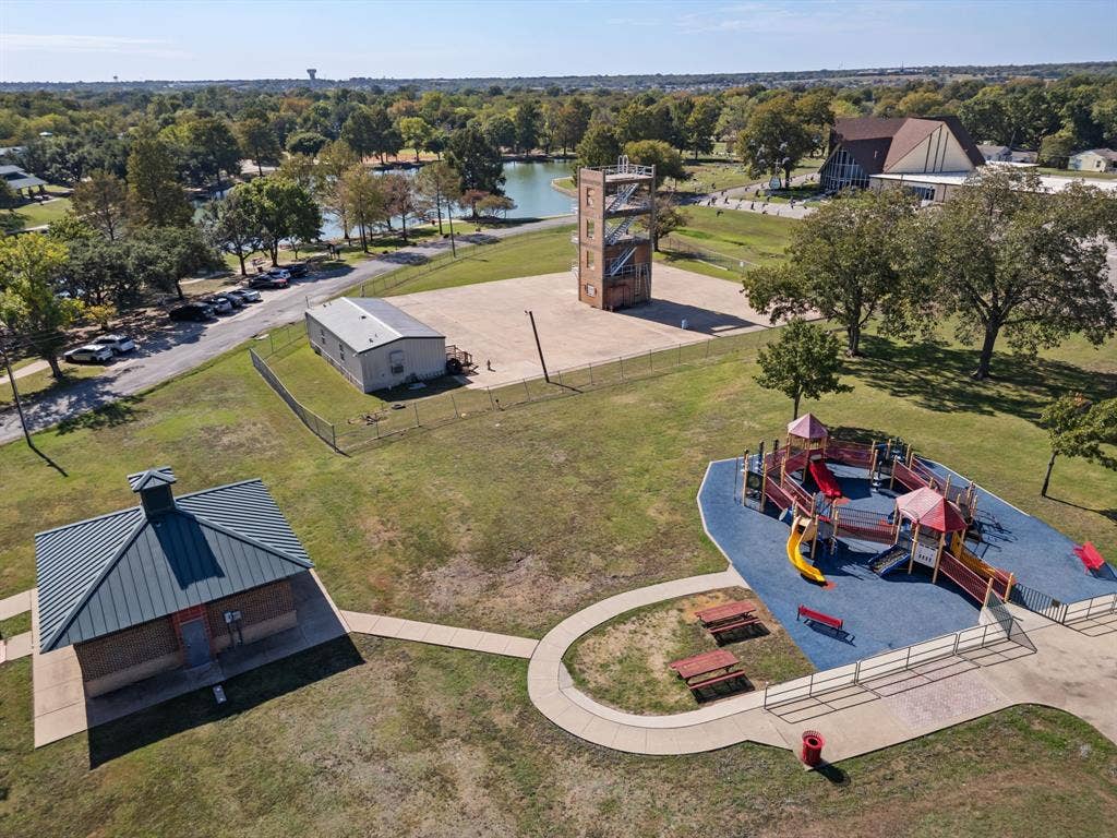 Outdoor recreational area featuring a playground with rubberized surfacing, a detached structure with a metal roof, concrete walkways, and open green space