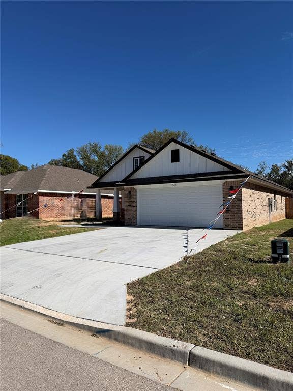 Single-story exterior featuring a brick and vertical siding facade, a dual-gabled roofline, and a paved concrete driveway leading to an attached two-car garage