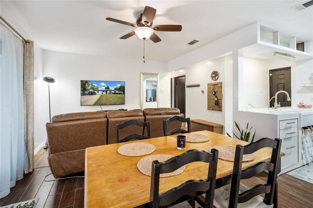 Wood-finish flooring, ceiling fan with integrated light fixture, and white cabinetry with a farmhouse sink